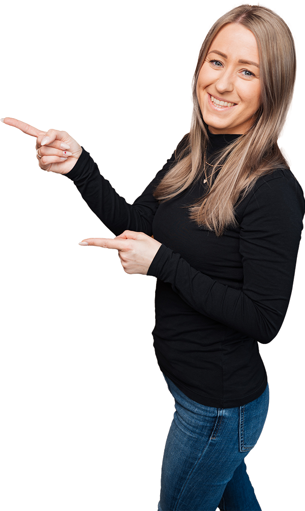 Eine lächelnde Frau mit glattem, hellbraunem Haar, die ein schwarzes, langärmeliges Oberteil und blaue Jeans trägt, steht vor einem weißen Hintergrund und zeigt mit beiden Händen nach links - perfekt, um für Wohnungsauflösung oder Altmöbelentsorgung zu werben.