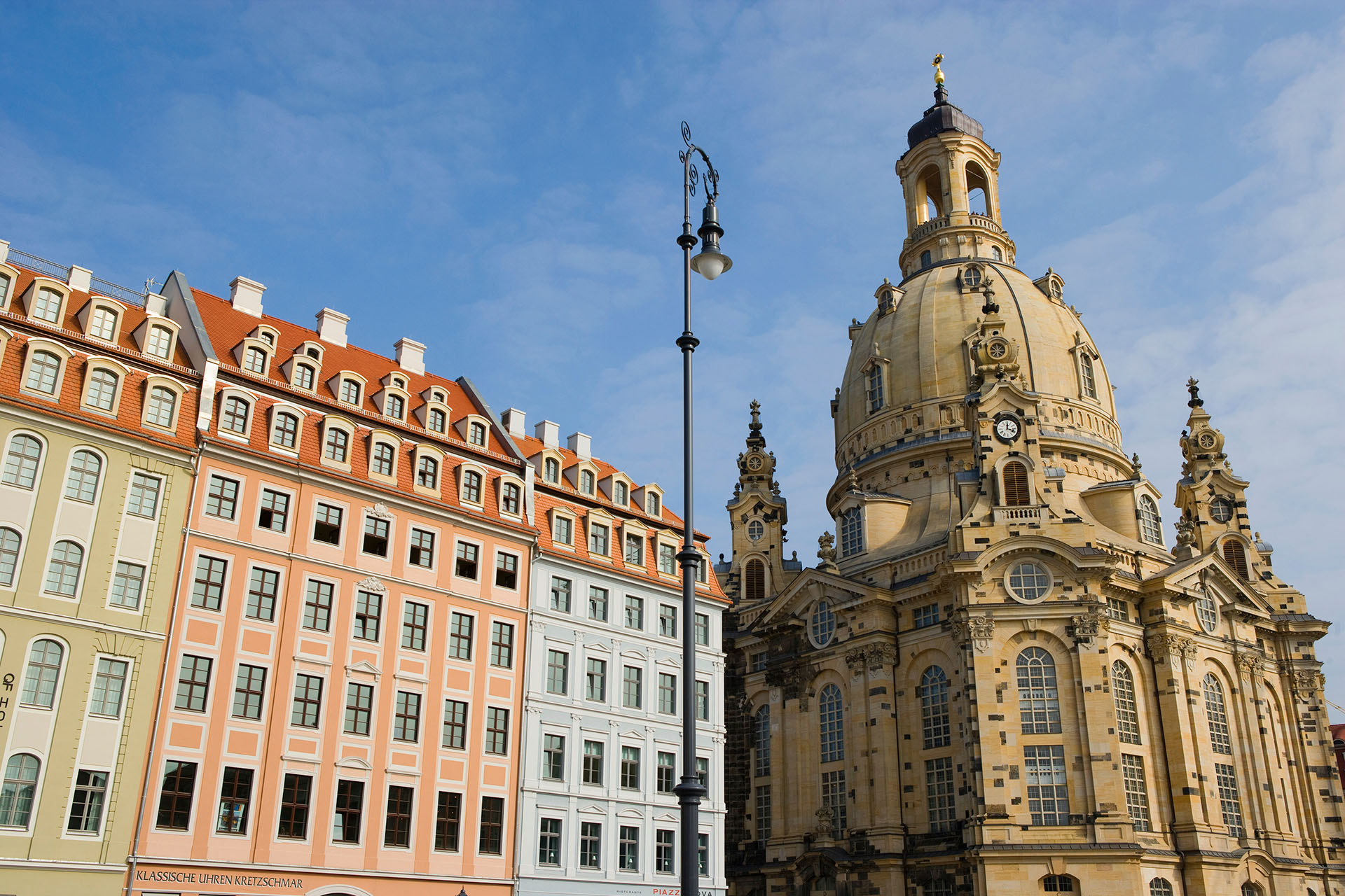 Bunte historische Gebäude und die prächtige Frauenkirche mit ihrer großen Kuppel stehen unter blauem Himmel in Dresden, Deutschland, wo Dienstleistungen wie die Wohnungsauflösung einen Umzug oder eine Entrümpelung stressfrei machen. Zwischen den Gebäuden ragt eine Straßenlaterne empor.