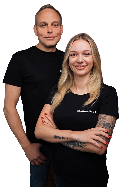 Ein Mann und eine Frau, beide in schwarzen "Räumweiß.de"-T-Shirts, stehen zusammen und lächeln vor einem schlichten weißen Hintergrund. Die tätowierte Frau verschränkt die Arme und steht für die Kompetenz von Räumweiß.de in Sachen Entrümpelung und Haushaltsauflösung.